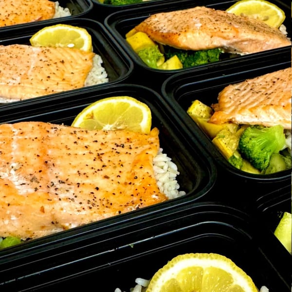 Multiple deli containers with salmon, rice, lemon, broccoli, and yellow squash.