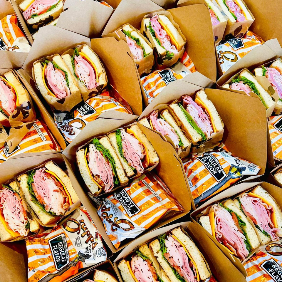 Numerous Flurry's Market deli sandwiches with chips, packaged in individual brown boxes for takeout.
